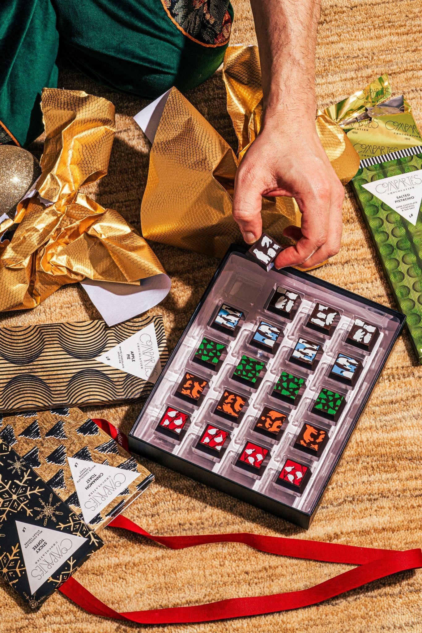 Christmas Chocolates being unwrapped and opened on a floor with Compartes Chocolate bars beside the box